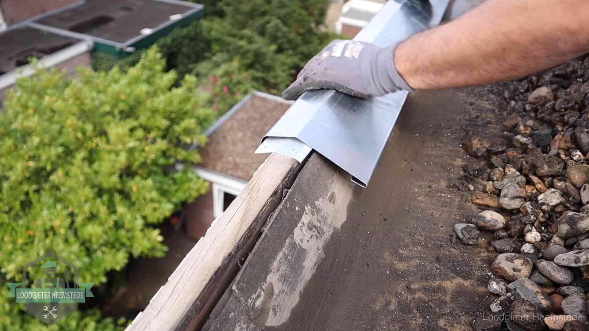 Dakdekker plaatst een zinken deklijst op een dakrand met uitzicht over een woonwijk in Heemstede