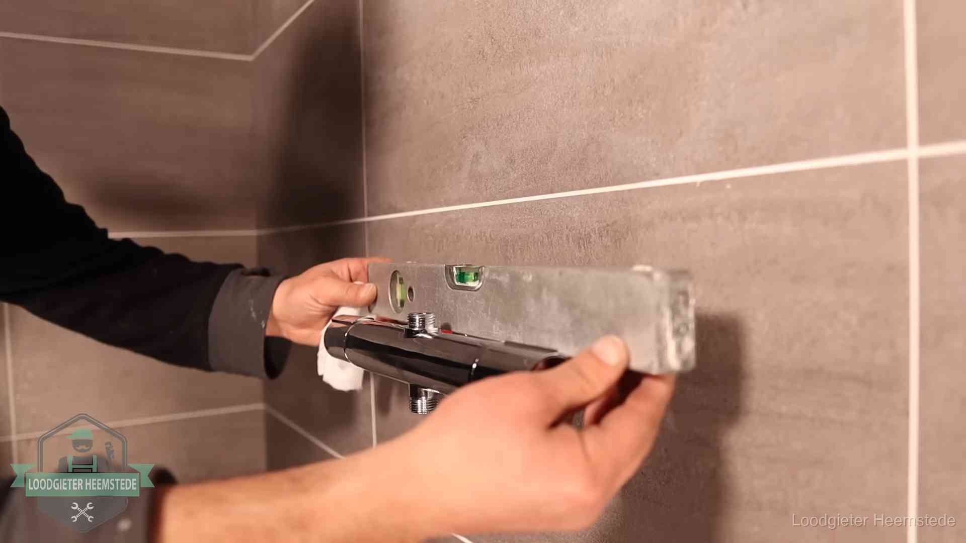 Loodgieter lijnt een douchekraan uit met een waterpas in een woning in Heemstede