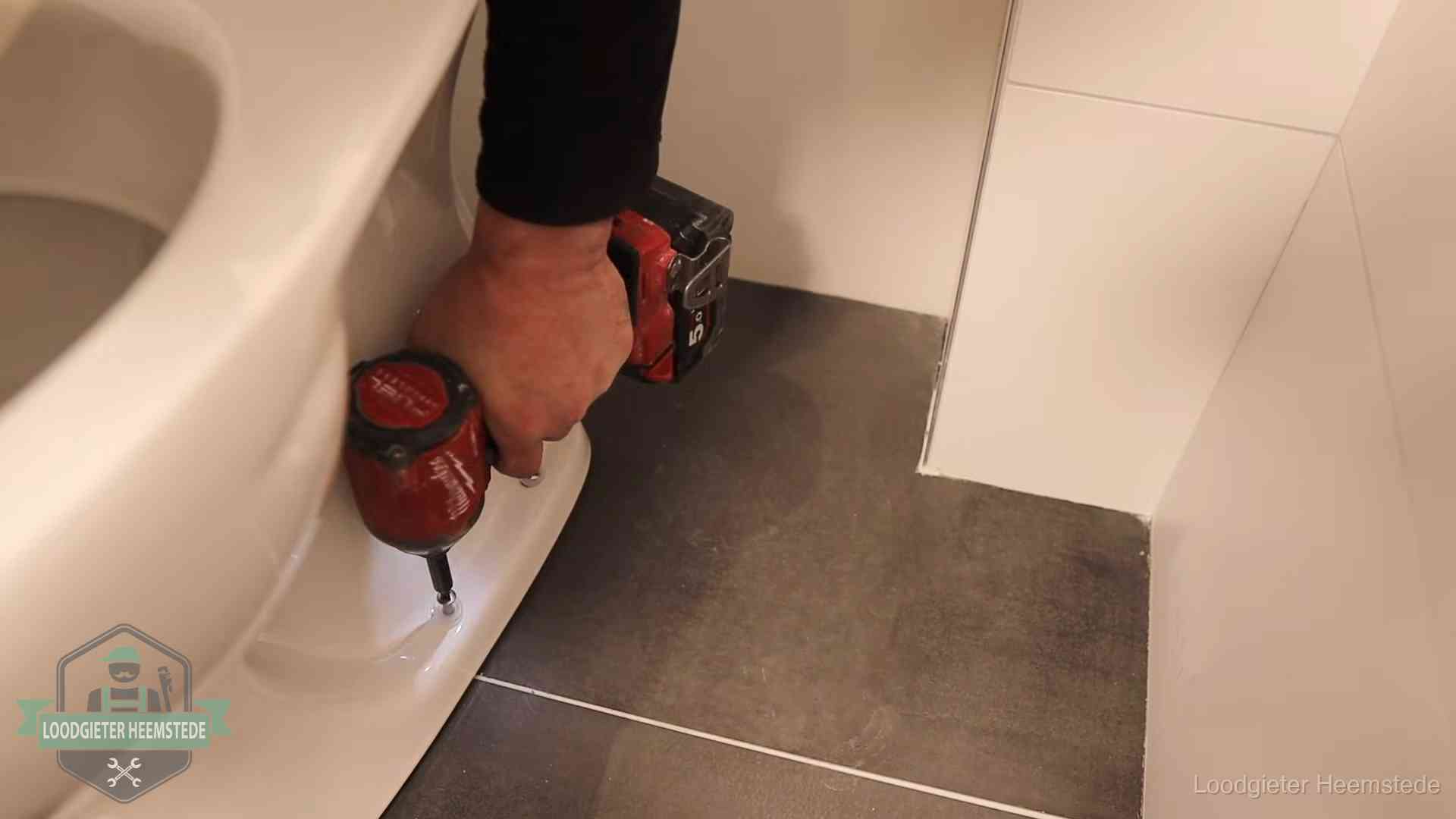 Kosten wc ontstoppen in Heemstede Loodgieter zet de voet van een wc-pot vast op de tegelvloer in Heemstede